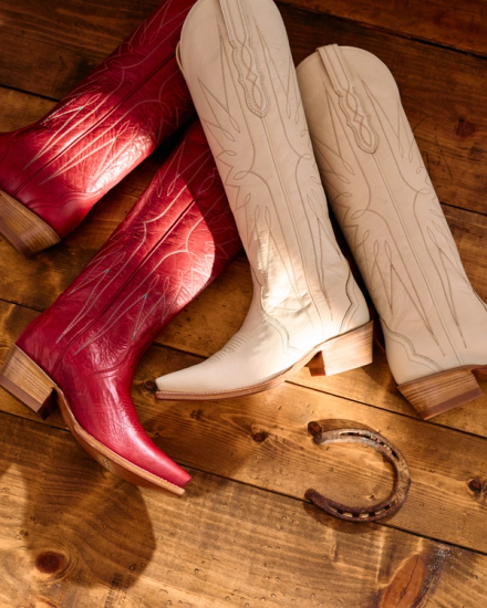 Two pairs of cowboy boots, one red and one white, are placed on a wooden floor beside a horseshoe.