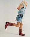 Young child wearing a denim shirt, denim shorts, and red cowboy boots runs against a plain light background.