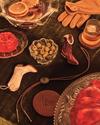 A table setting with gloves, olives, orange slices, a drink, two cowboy boot-shaped ornaments, a bolo tie, leather coaster, and red gelatin dessert on a velvet tablecloth.