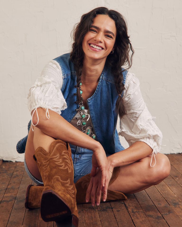 A woman sitting on the floor in cowboy boots.