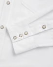 Close-up of a white long-sleeve shirt featuring metal snap buttons on the cuff and front placket, along with a visible chest pocket seam.