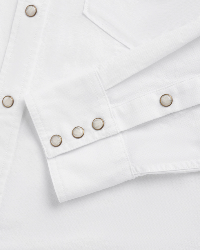 Close-up of a white long-sleeve shirt featuring metal snap buttons on the cuff and front placket, along with a visible chest pocket seam.