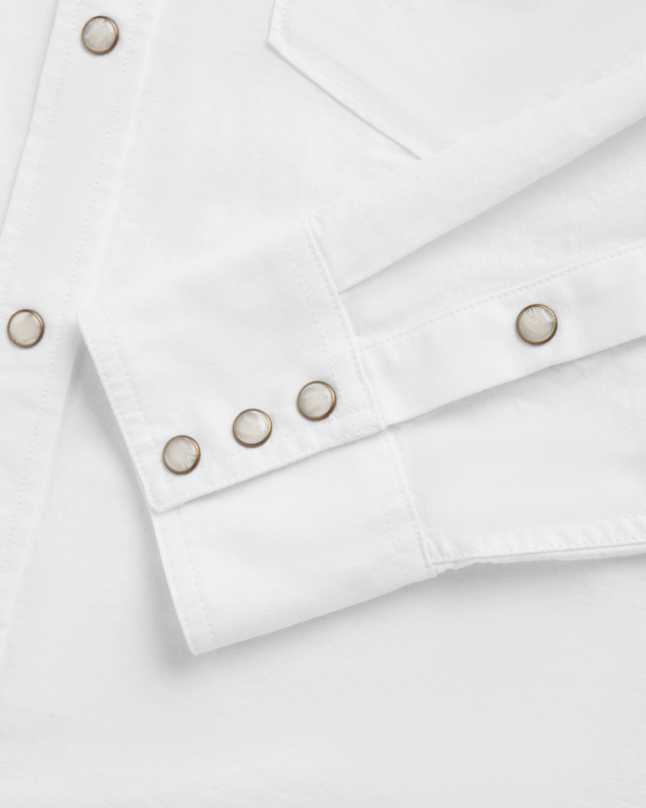 Close-up of a white long-sleeve shirt featuring metal snap buttons on the cuff and front placket, along with a visible chest pocket seam.