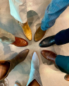 Six people standing in a circle, showcasing a variety of stylish shoes in different colors and textures on a concrete floor.