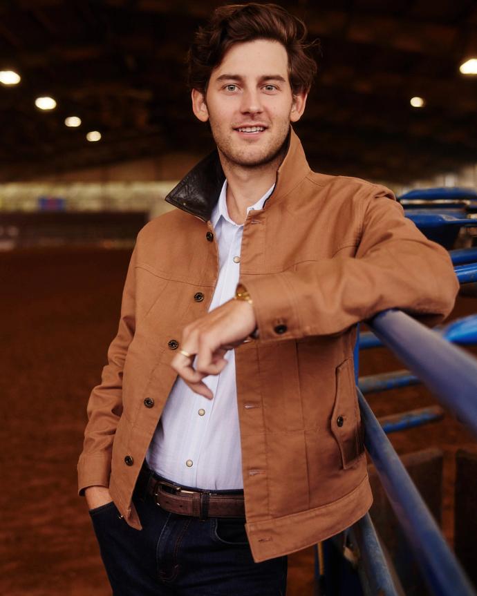 Man wearing brown jacket leaning on fence smiling 