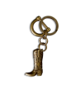 A brass keychain featuring a small, detailed cowboy boot charm with engraved patterns, set against a black background.