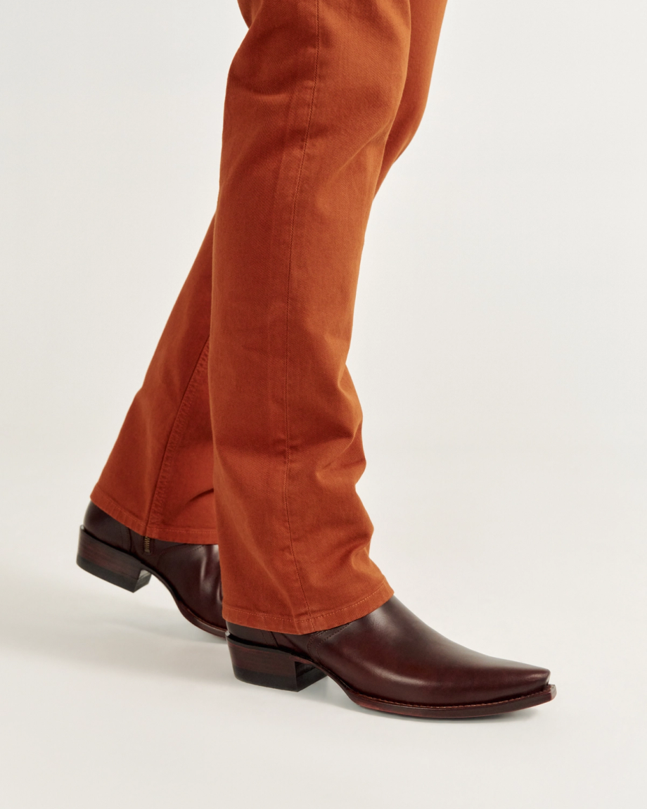 Person wearing orange pants and brown leather boots against a plain background.