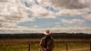 Man wearing a cowboy hat in a field fixing a fence.