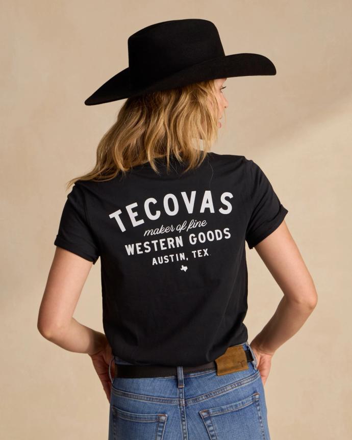 Person wearing a black cowboy hat and a black T-shirt with "Tecovas, maker of fine western goods, Austin, Tex." on the back.