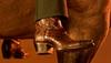 Close-up of a person wearing brown crocodile-patterned leather cowboy boots, with legs draped over the side of a horse.