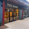 Storefront of a Tecovas shop with illuminated sign and visible interior display, featuring a modern exterior design with red structural accents.