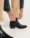 Person wearing beige pants, adjusting black textured leather boots with a side zipper.