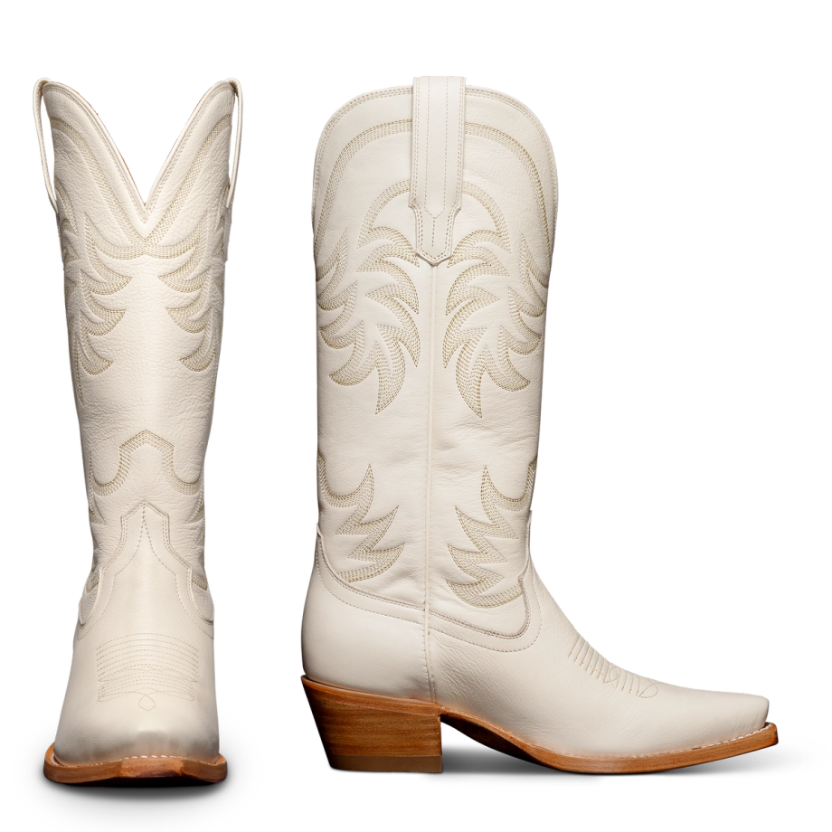 Two white cowboy boots with decorative stitching, showing side and rear views. They have brown stacked heels and pointed toes.