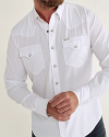 Man in a white button-up shirt with two flap pockets and metal buttons stands with arms crossed.