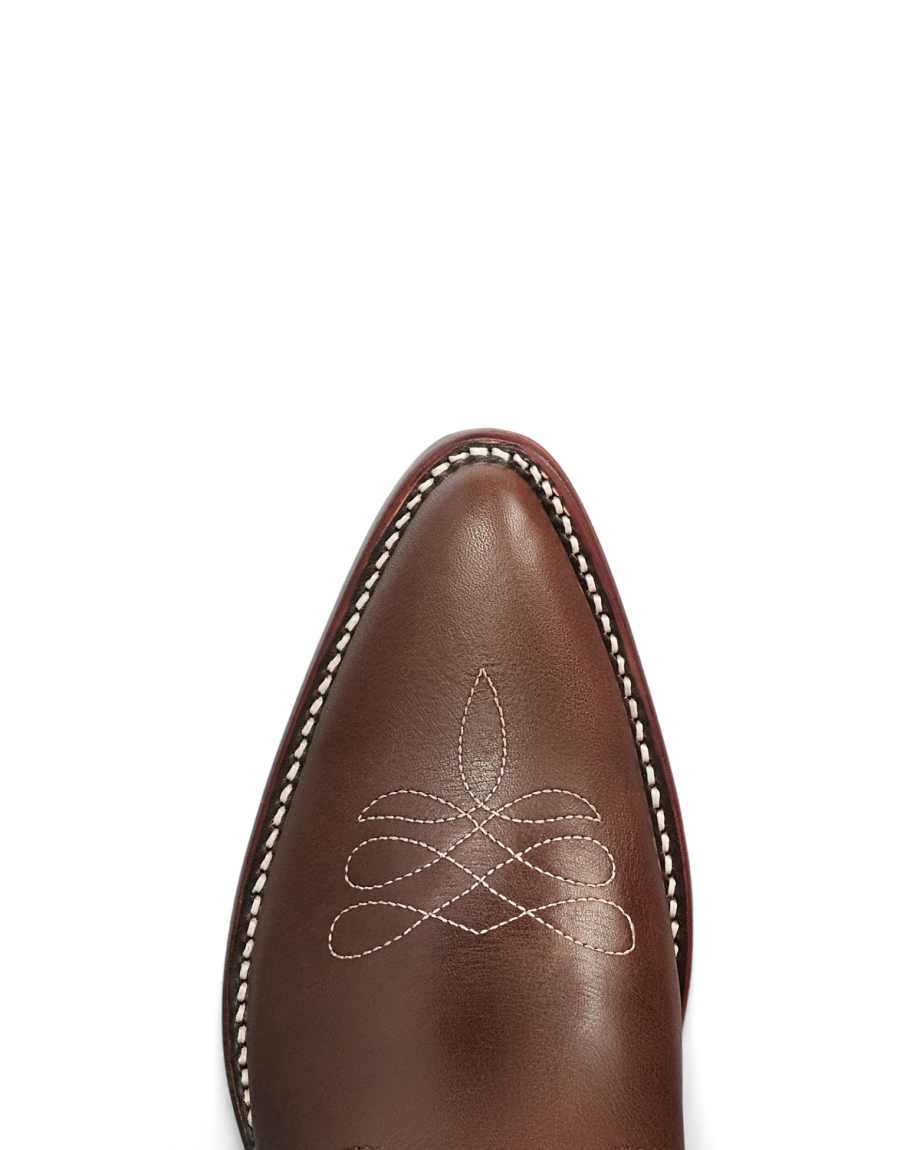 The Jolene in Truffle Cowhide. Close-up of the pointed toe of The Jolene Cowhide brown leather cowboy boot with white decorative stitching and a white-stitched welt, against a plain background.