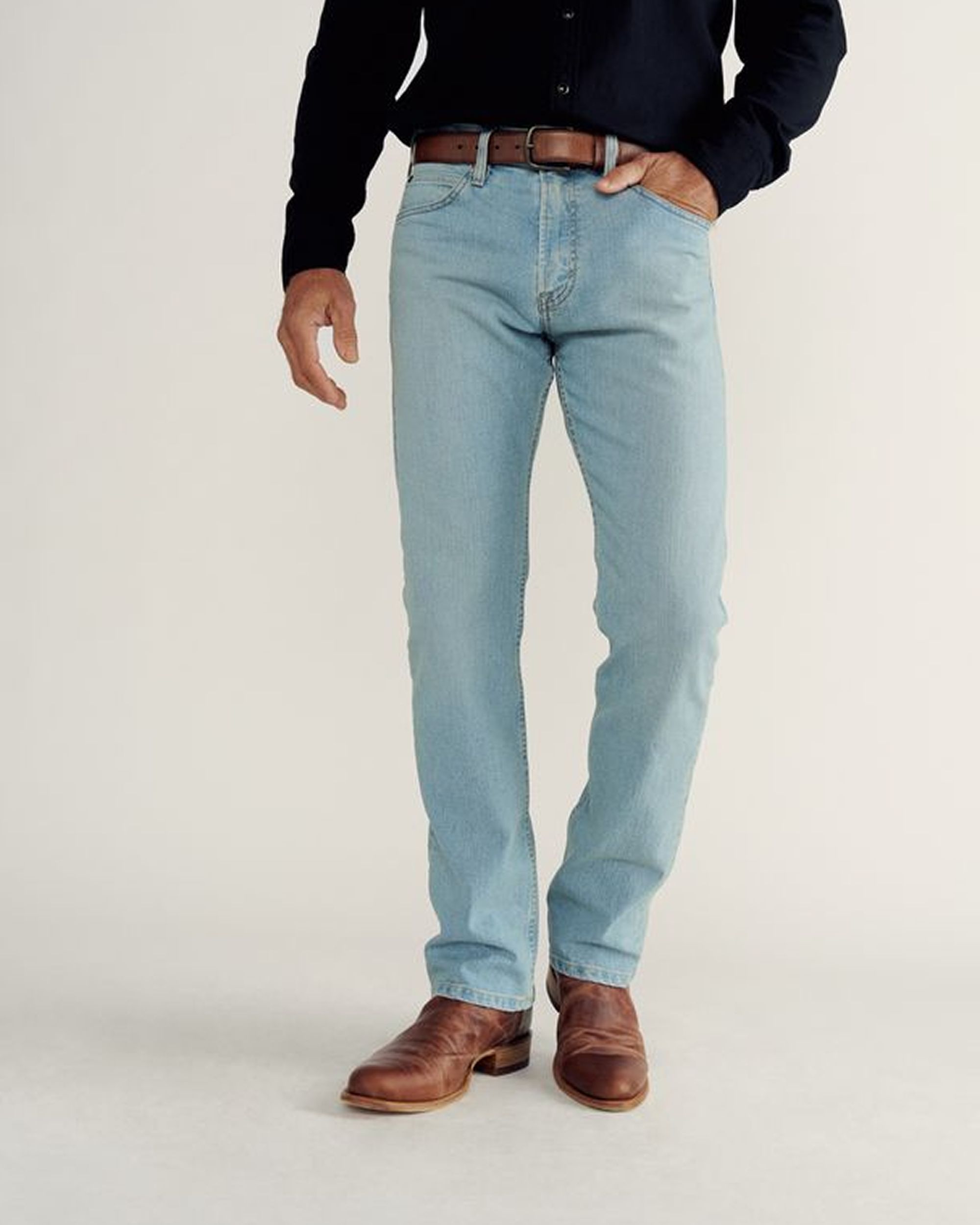 A person wearing a white t-shirt, blue jeans, and brown boots stands against a plain background.