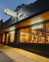 A cowboy boot store with a neon sign "Good Times" and "Come find your favorite boots" at night, featuring large windows displaying merchandise.