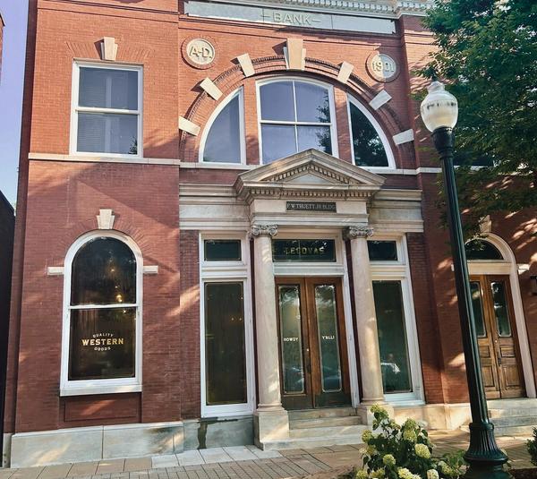 A historic red brick building with arched windows, a sign reading "BANK" above the entrance, and a streetlamp in front.