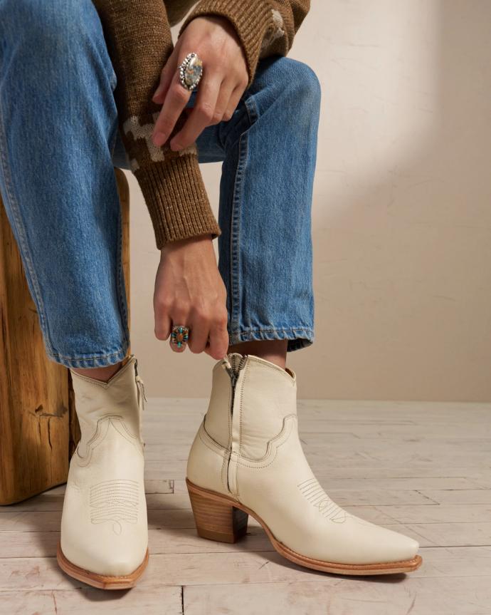 Woman zipping up white ankle boots in a photo studio