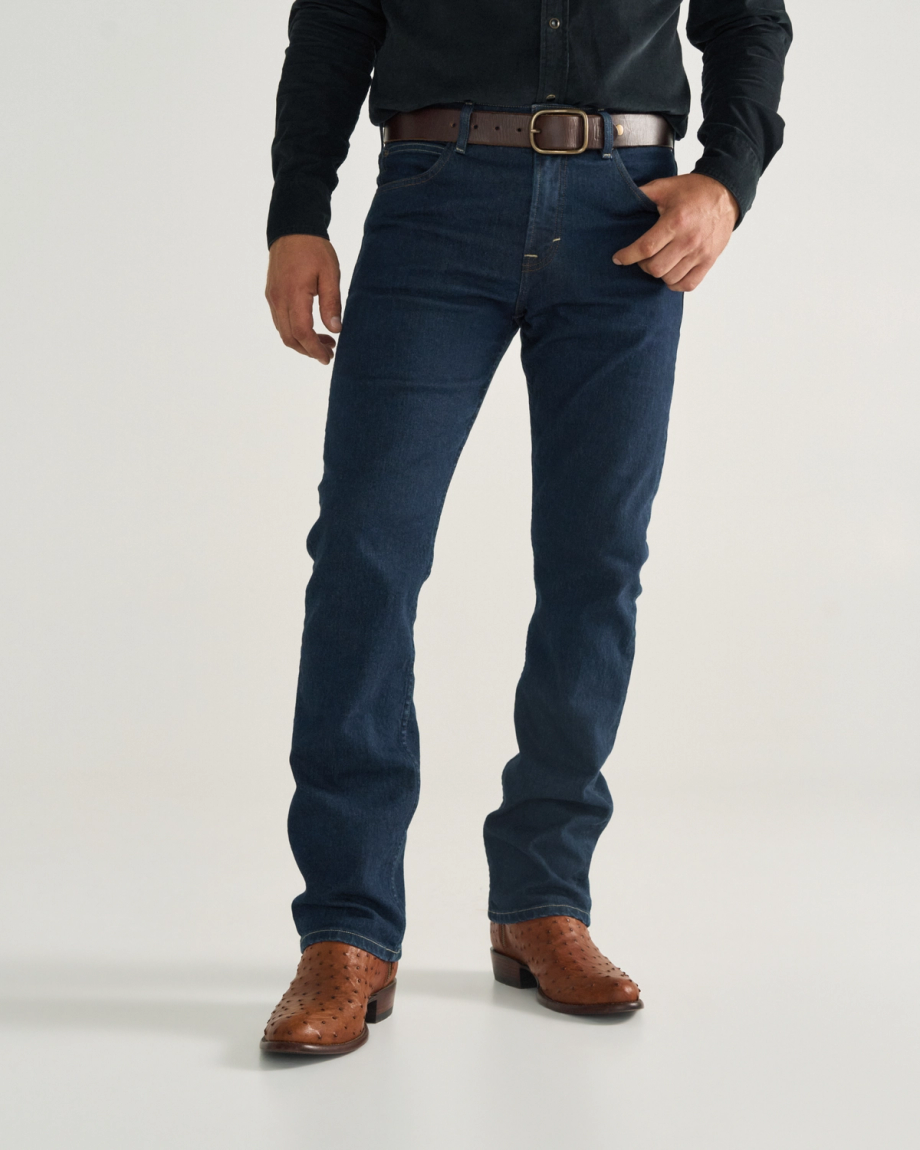The Dean in Pecan Ostrich. A man wearing a black shirt, brown belt, dark blue jeans, and pecan ostrich cowboy boots stands against a plain background.