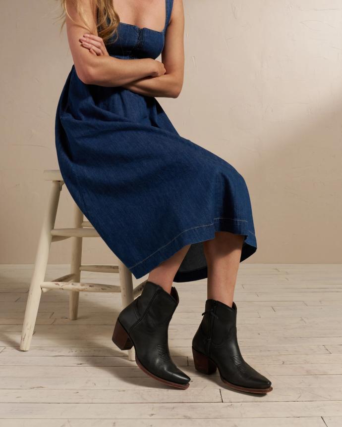 Woman in a denim dress and black booties sitting in a photo studio