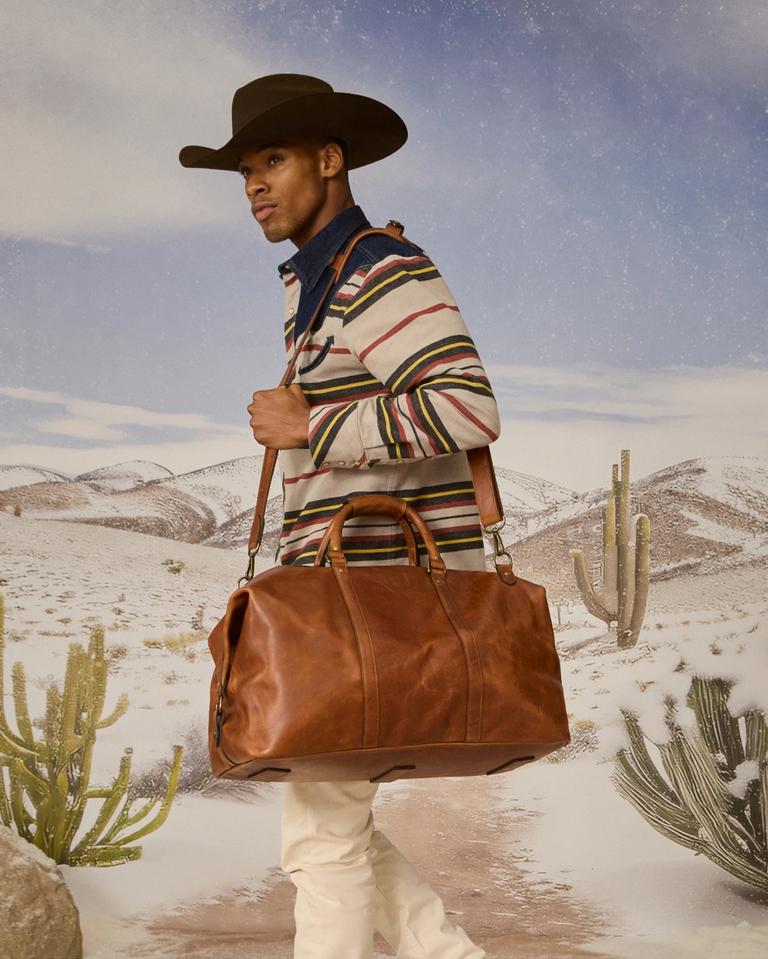 Man wearing cowboy hat, western shirt and carrying a leather travel bag.