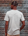 Man wearing the standard issue pocket tee in heather grey against a rustic wall