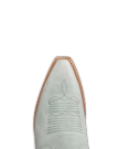 The Annie in Slate Blue Cowhide. Close-up of the pointed toe of a light gray western-style boot with decorative stitching and a tan welt.