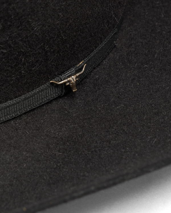 Close-up of a black felt hat with a black ribbon band and a small metallic longhorn ornament attached to the band.