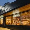 Storefront of Tecovas at dusk with illuminated signs reading "Good Times" and "Western Goods," showing boots and hats displayed inside through large windows.