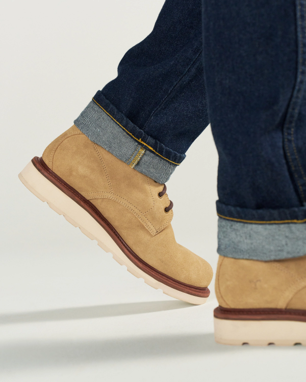The Knox Lace Up Shearling in Sandstone Roughout. Person wearing rolled-up dark blue jeans and tan Sandstone Roughout lace-up shoes with white soles, shown from the lower leg down.