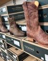 A row of brown leather cowboy boots displayed on Tecovas shoe boxes in a store.