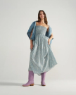 The Annie in Lavender Suede. A woman wearing a blue floral dress, a denim jacket draped over her shoulders, and Lavender Suede boots stands against a plain light background.