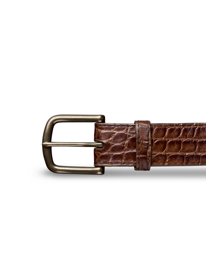 Brown leather belt with a crocodile texture and a brass buckle on a black background.