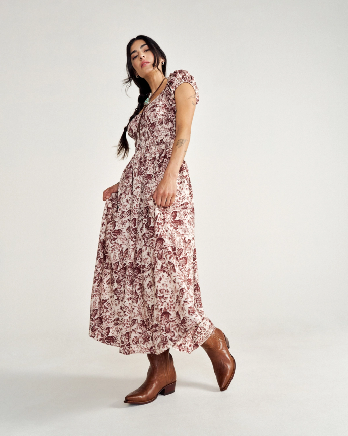 A person wearing a patterned long dress and brown cowboy boots stands against a plain background.