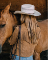 Person in a fringed brown jacket and cowboy hat standing next to a horse.