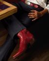 A person wearing dark pants, a red belt with a silver buckle, and red cowboy boots sits with legs crossed beside a wooden table.
