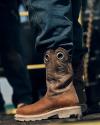 Close-up of a person wearing brown leather cowboy boots and blue jeans, standing on a textured surface.