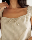 A woman wearing a beige and white striped sleeveless top with lace-trimmed straps and buttons on the front. Only her torso and part of her arm are visible.