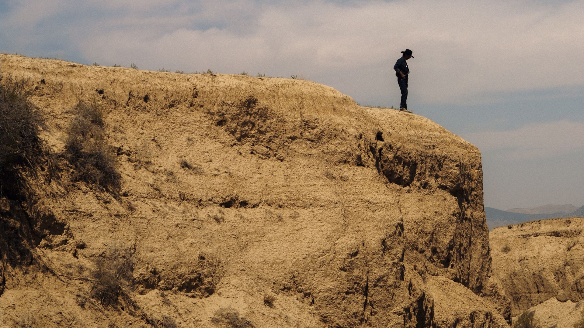 A person in a cowboy hat standing on the edge of a desert cliff.
