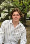A young man in a striped shirt leaning against a tree.