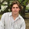 A young man in a striped shirt leaning against a tree.