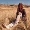 Woman sitting in a field wearing white boots and dress