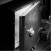 A black and white photo of an open, empty safe with a combination lock.