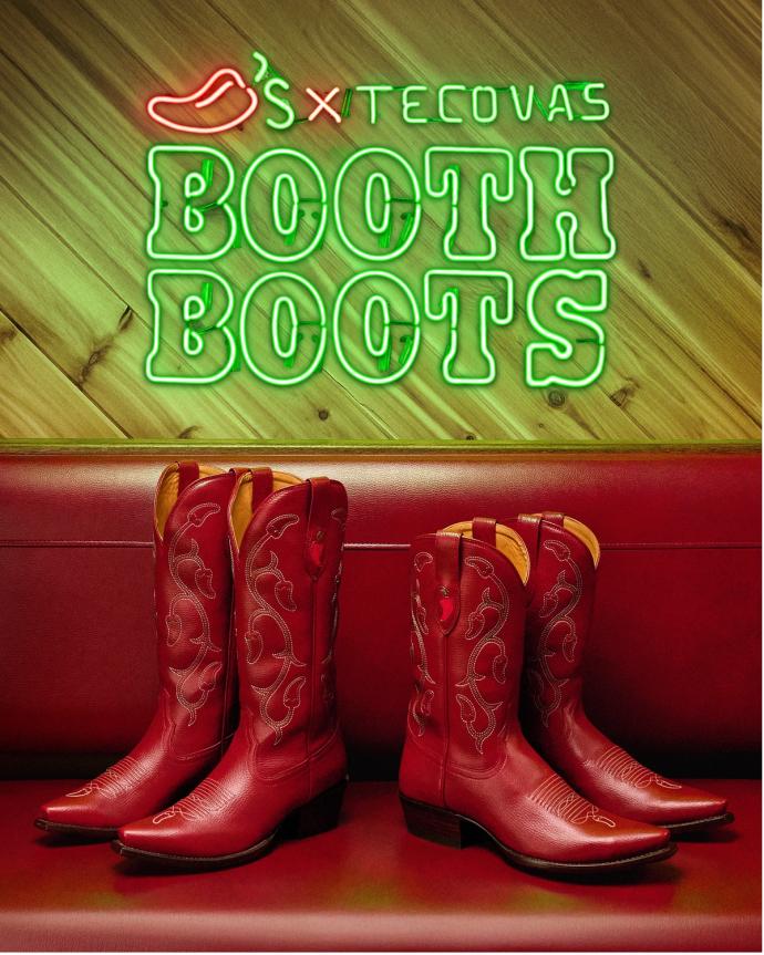 Two pairs of red cowboy boots are displayed on a red bench below a neon sign that reads "S X Tecovas Booth Boots" with a chili pepper graphic.