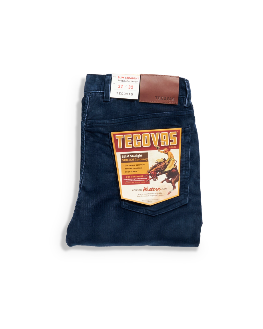 A pair of folded dark blue corduroy pants with a brown leather patch on the waistband, displayed on a light background.