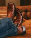 A person wearing textured brown leather cowboy boots, crossed at the ankles, sits relaxed on a leather sofa.