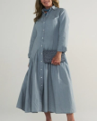 A woman wearing a long-sleeved, light blue button-down dress is holding a gray textured clutch bag.