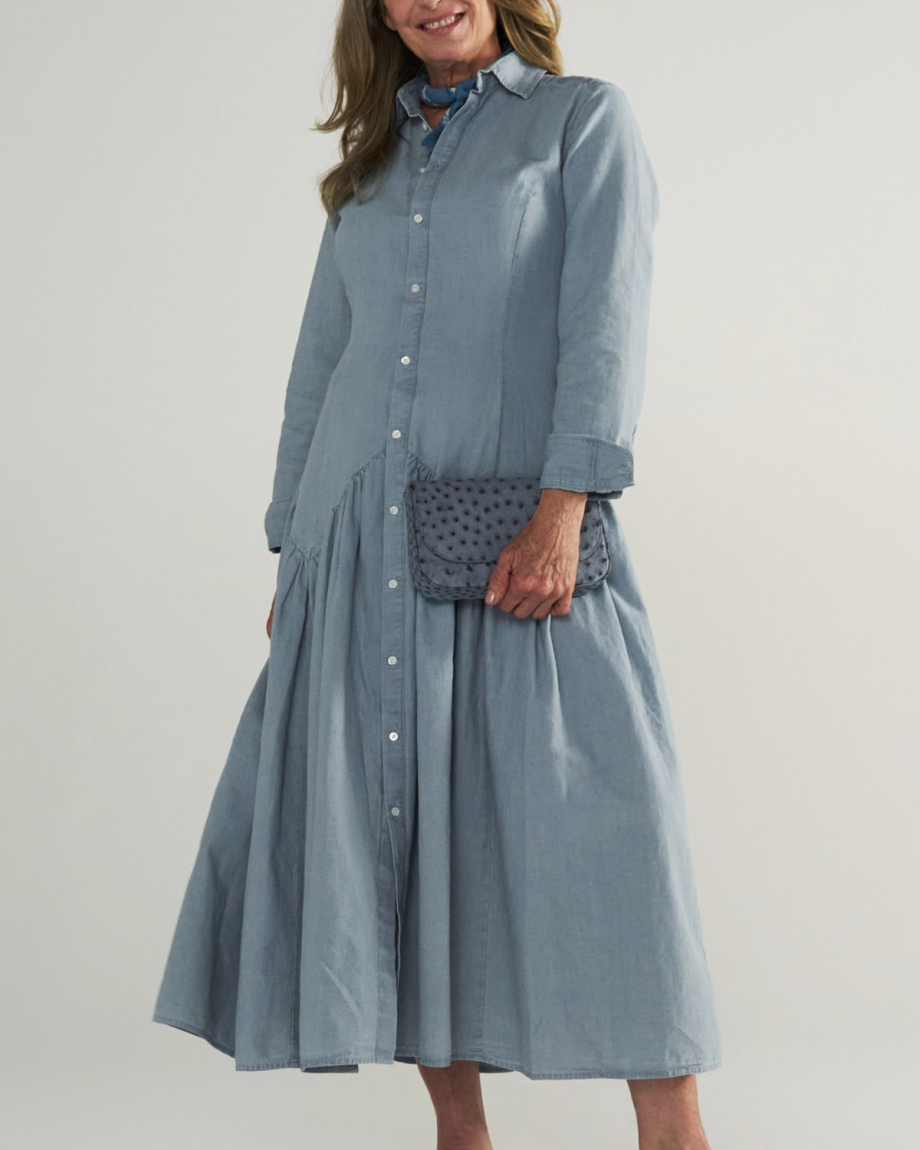 A woman wearing a long-sleeved, light blue button-down dress is holding a gray textured clutch bag.