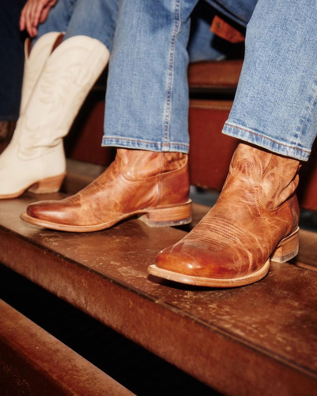 Two people wearing cowboy boots sitting on wooden steps, with focus on the detailed texture and design of the boots.